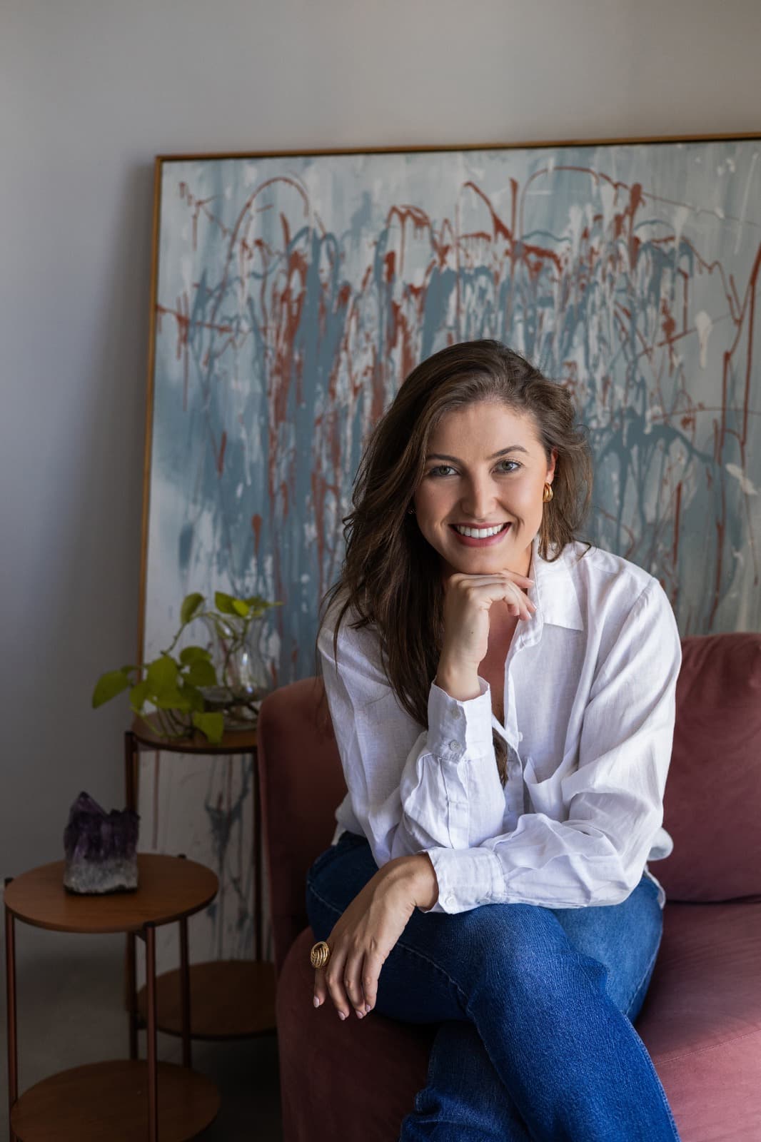 Arquiteta Alessandra Arnhold sentada num sofá rosé, sorrindo, com a mão apoiada no queixo