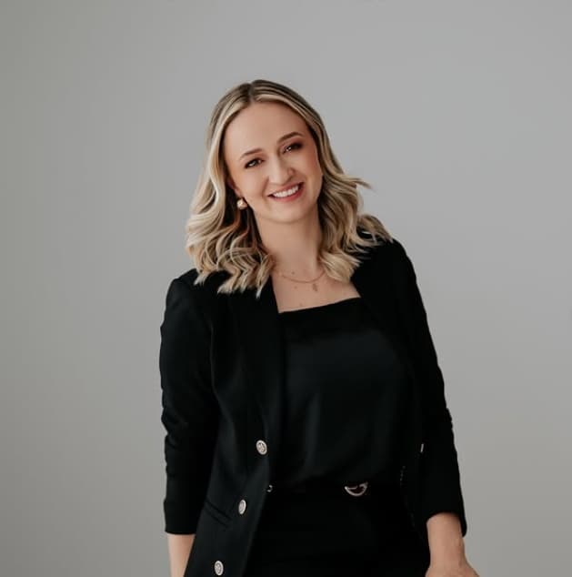 Arquiteta Gabriela Wietholder de blazer preto, sorrindo, diante de um fundo cinza-claro